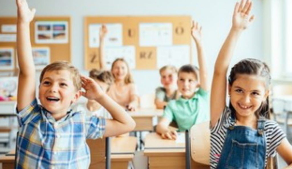 Bambini nei banchi di scuola alzano la mano